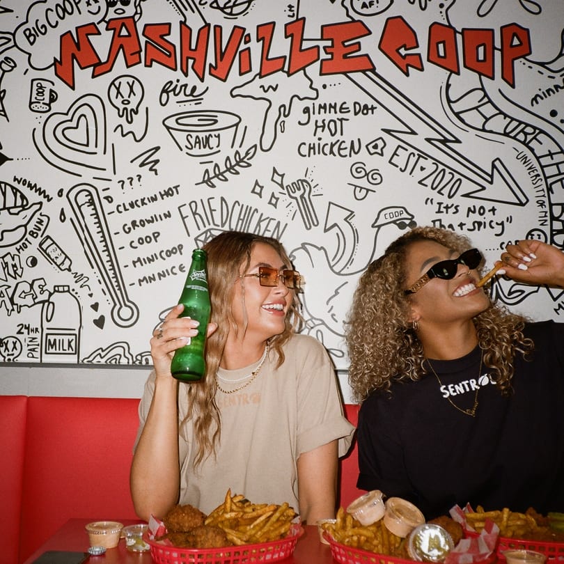 Two women enjoying Nashville Coop fried chicken and fries at a red booth with a doodle wall.
