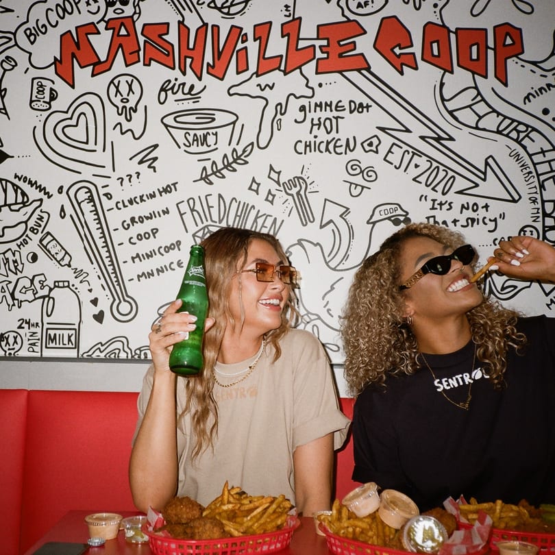 Two women enjoying Nashville Coop fried chicken and fries in a booth with a doodle-covered wall.