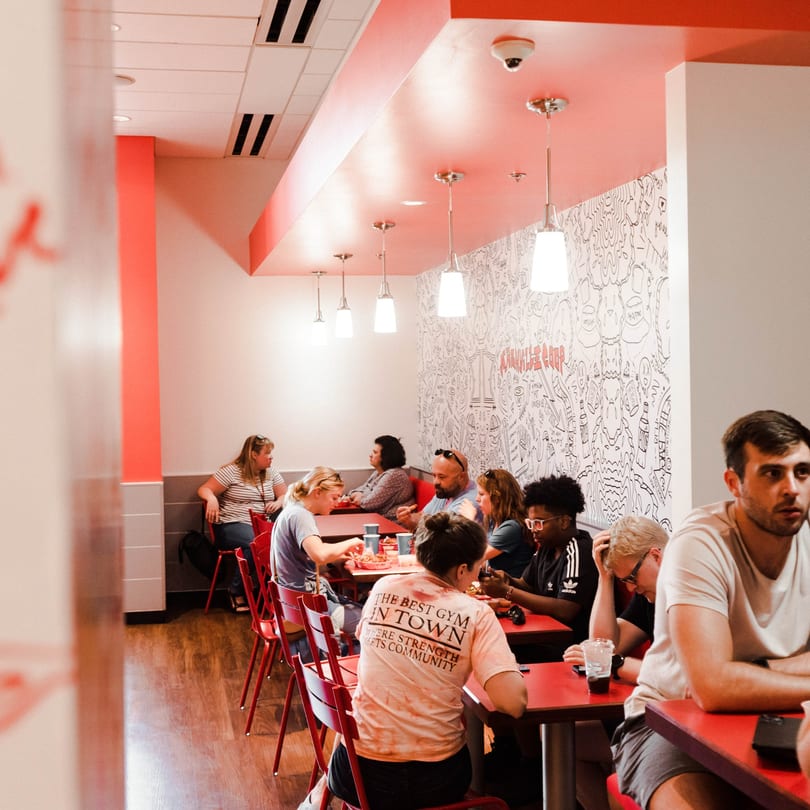 Customers dining at red tables in a Nashville Coop restaurant with a doodle-covered wall.
