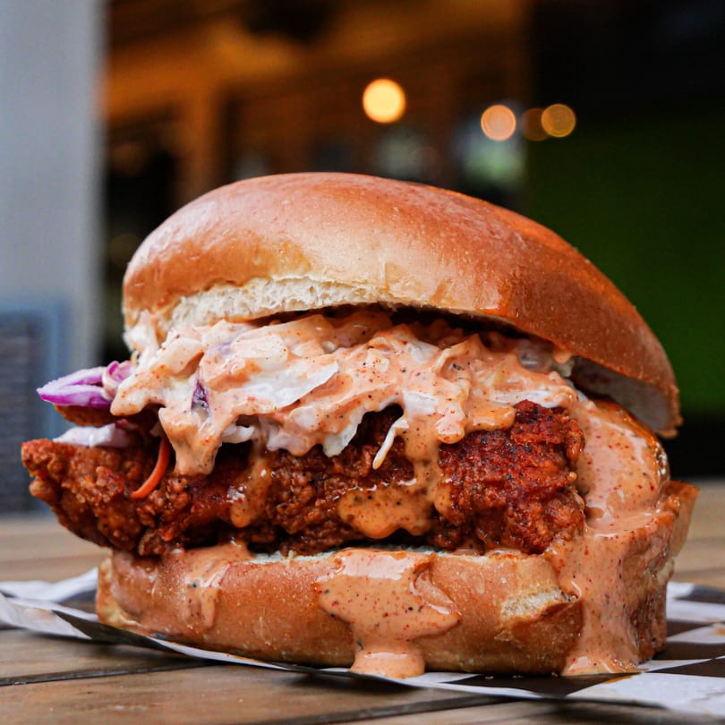 Nashville Coop's fried chicken sandwich with coleslaw, red onions, and spicy sauce on a bun.