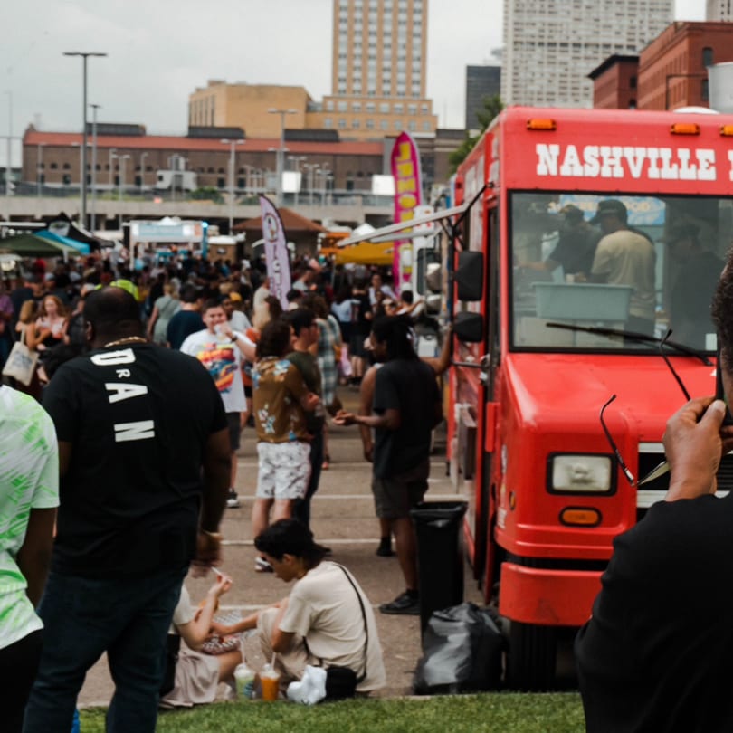 A red Nashville Coop food truck at a busy outdoor market with people milling around.