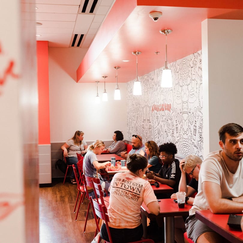 Diners enjoying meals at red tables in a Nashville Coop restaurant with doodle-covered walls.